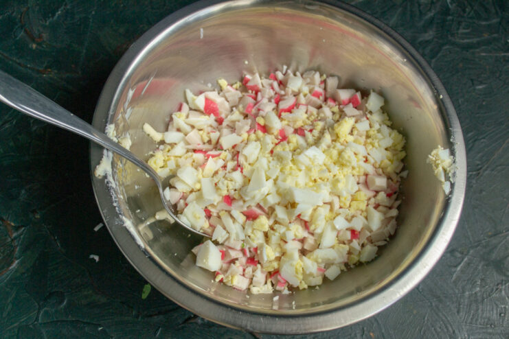Adding finely chopped hard-boiled eggs for extra richness and texture. Finely chopped hard-boiled eggs being added to a bowl of crab sticks and cheese.
