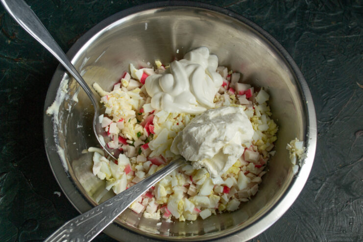 The combination of smetana and cream cheese creates a rich and creamy dressing. Spoons of smetana and cream cheese being added to the bowl of ingredients.