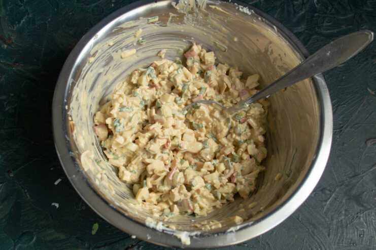 Stir everything together until well combined and creamy. A spoon mixing the crab stick appetizer ingredients in a glass bowl.