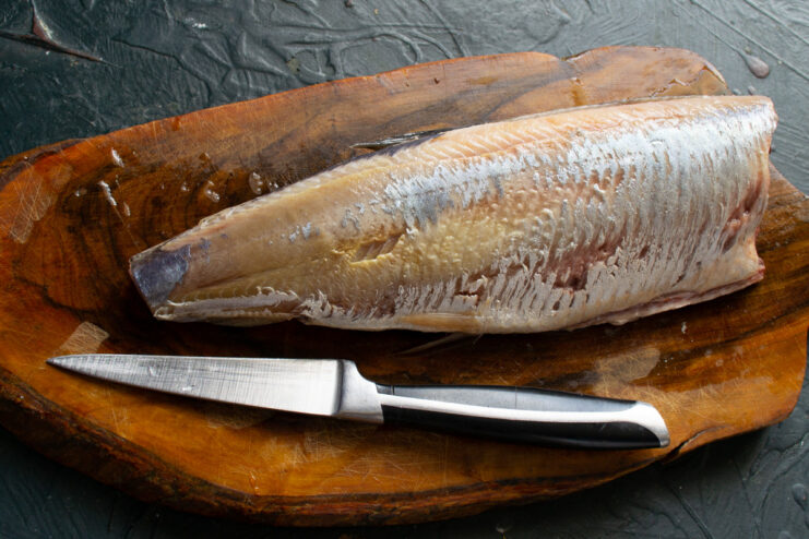 How to properly clean and prepare a whole herring for filleting A whole herring on a cutting board being cleaned and prepared for filleting.