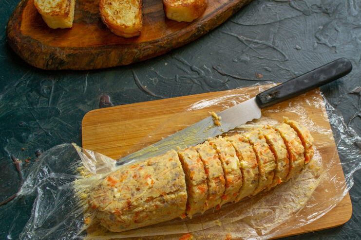 Slicing the chilled herring pâté log into rounds A chilled log of herring pâté being sliced into thick rounds on a cutting board.