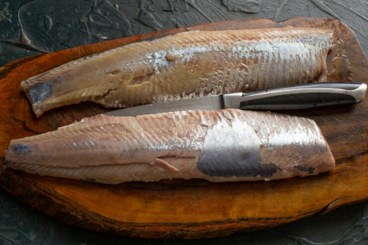 Using tweezers to remove fine bones from herring fillets Two herring fillets being deboned with tweezers on a cutting board.