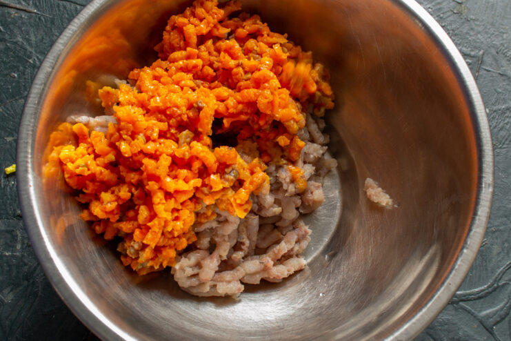 Adding cooked carrots to the herring in the meat grinder Cooked and cooled carrots being added to a meat grinder after the herring.