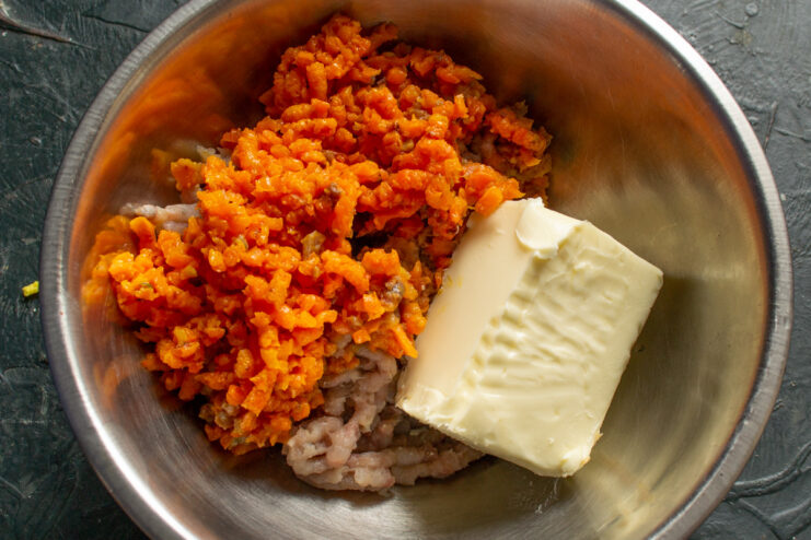 Combining ground herring and carrots with softened butter A bowl with ground herring and carrots, with a block of softened butter being added.