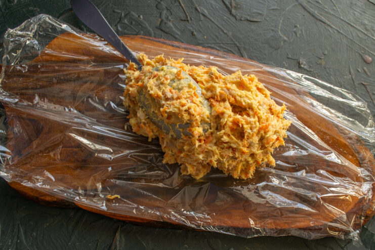 Spreading the herring pâté onto plastic wrap for shaping Herring pâté being spread onto a sheet of plastic wrap on a cutting board.
