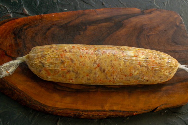How to shape herring pâté into a log using plastic wrap A long log of herring pâté being tightly wrapped in plastic wrap.