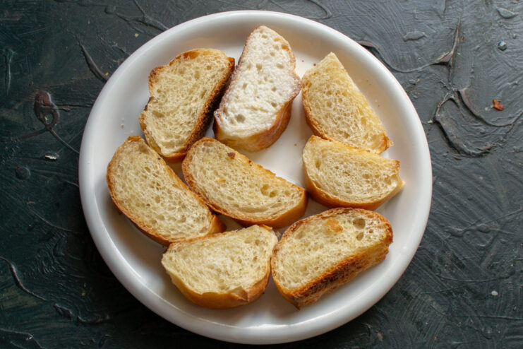 Soaking baguette slices in milk for tender croutons Sliced baguette in a white bowl, with milk being poured over it.