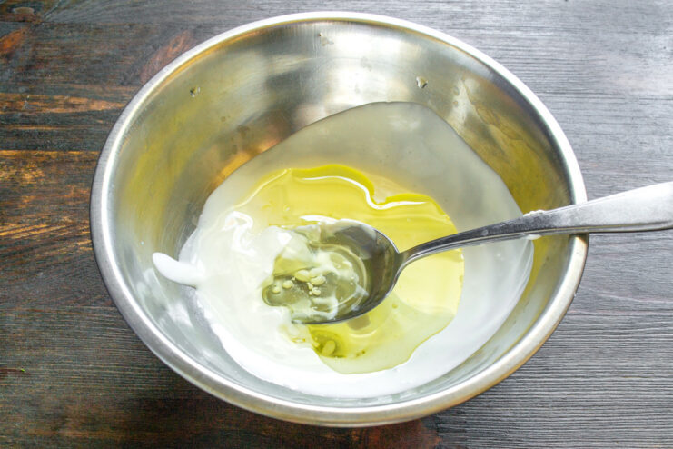 Creating the Wet Base: Mixing Smetana and Cold-Pressed Olive Oil A white bowl containing smetana (sour cream) and olive oil being mixed together.