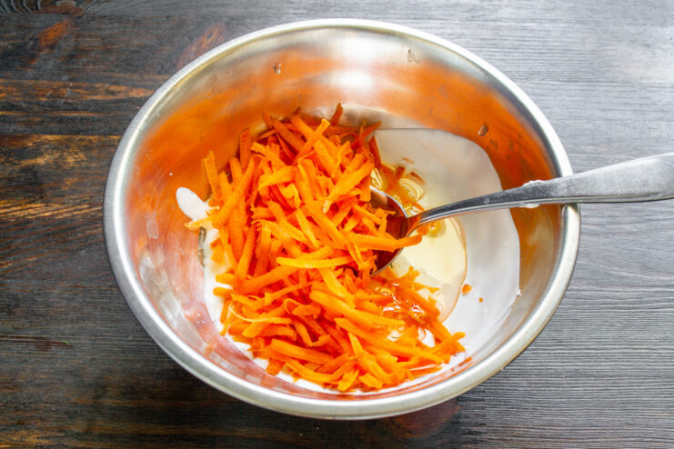 Adding Grated Carrots for Sweetness and Moisture Grated carrots being added to the wet ingredients in a mixing bowl.