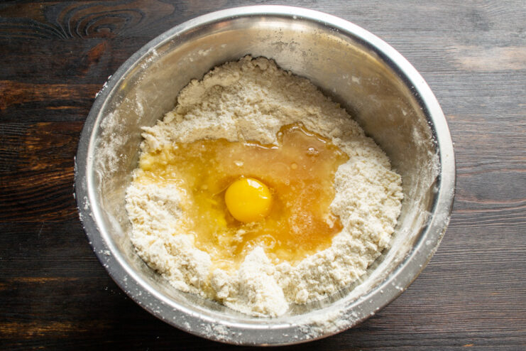 Adding an Egg to the Dough A chicken egg being cracked into the bowl with the flour and butter mixture.