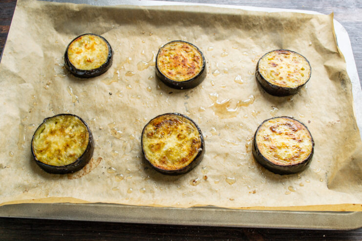 Baking the eggplant slices until they are tender and lightly golden. Golden-brown baked eggplant slices on a parchment-lined baking sheet.