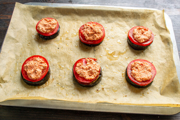 Adding a creamy farmer's cheese mixture to the tomato-topped eggplant. A spoonful of farmer's cheese mixture being placed on top of tomato slices on eggplant.
