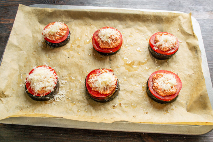 Sprinkling with Parmesan cheese for a savory, golden crust. Grated Parmesan cheese being sprinkled over the farmer's cheese topping on the eggplant stacks.
