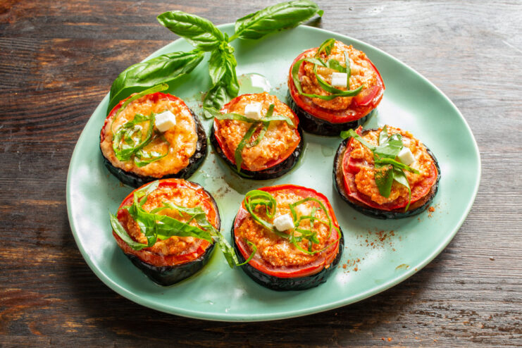 Garnishing the finished baked eggplant with fresh basil for extra aroma. Finished baked eggplant stacks being garnished with freshly chopped basil.