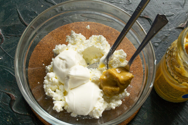 Step 2: Adding smetana or yogurt for extra creaminess. Adding a spoonful of smetana or yogurt to the bowl with curd cheese.