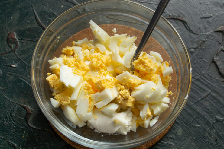 Step 3: Incorporating diced hard-boiled eggs into the salad base. Diced hard-boiled eggs being added to the bowl with the cheese and smetana mixture.