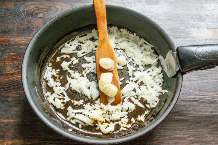 Sautéing Onions and Garlic to Build Flavor Diced onions and sliced garlic being sautéed in a hot frying pan with oil.