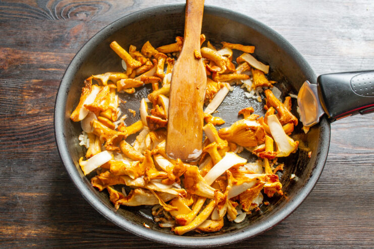 Combining Chanterelles with Sautéed Onions Chopped chanterelle mushrooms being added to a pan with sautéed onions and garlic.
