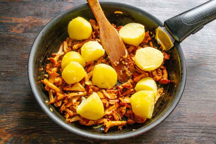 Adding Potatoes to the Chanterelle Mixture Halved boiled potatoes being added to a frying pan with cooked chanterelle mushrooms.