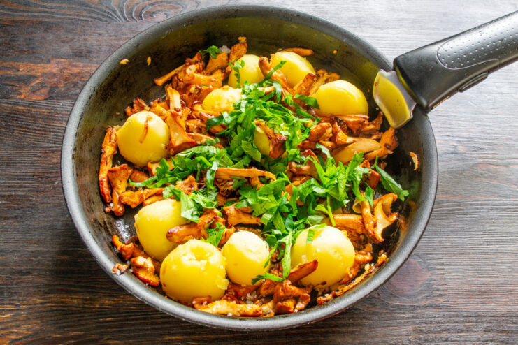 Finishing the Dish with Fresh Herbs Finely chopped parsley being sprinkled into a pan with fried chanterelles and potatoes.