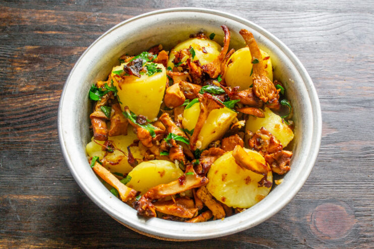 The Perfect Rustic Serving Suggestion for Fried Chanterelles A rustic dinner setting with fried chanterelles and potatoes, served with rye bread, smetana, and green onions.