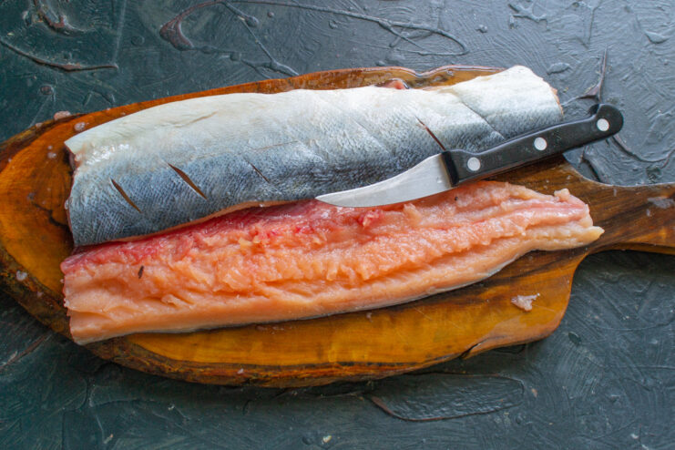 Step 2: Filleting the Salmon for Even Cooking Hands carefully filleting a salmon, separating the flesh from the spine with a knife.