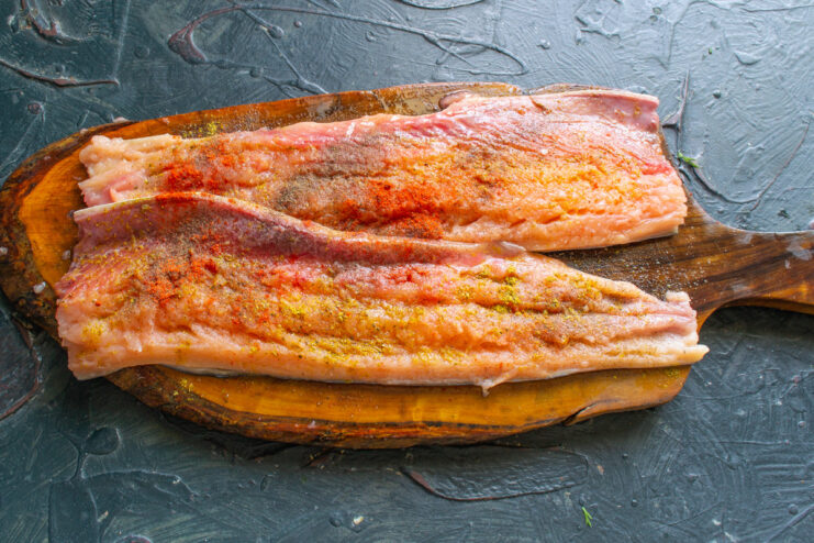Step 3: Seasoning the Salmon Fillets for Maximum Flavor Salmon fillets on a cutting board being seasoned with paprika, pepper, and other spices.