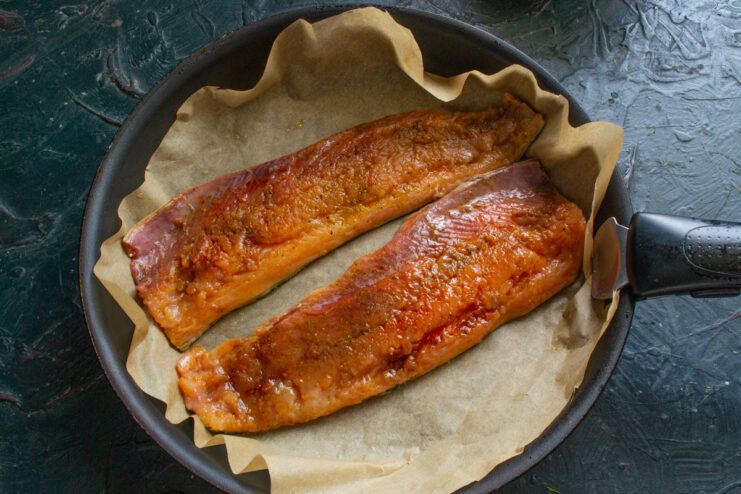Step 5: Cooking the Salmon on Parchment Paper A marinated salmon fillet being placed skin-side down onto parchment paper in a hot skillet.