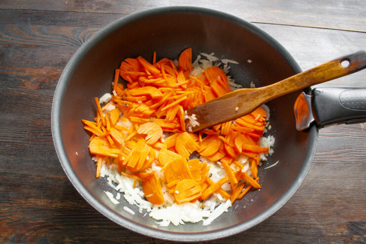 Adding Julienne Carrots to the Sautéed Onions Julienned carrots being added to a pan with sautéed onions and garlic.