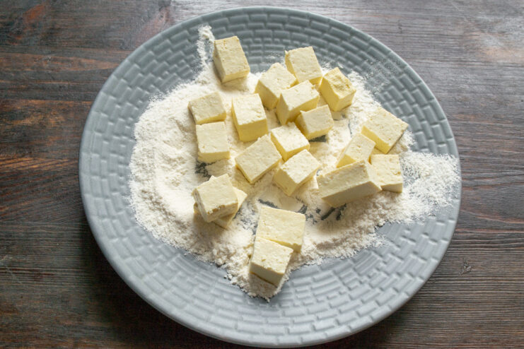 Coating Tofu Cubes in Flour Before Frying Cubes of tofu being coated in a bowl of white flour.