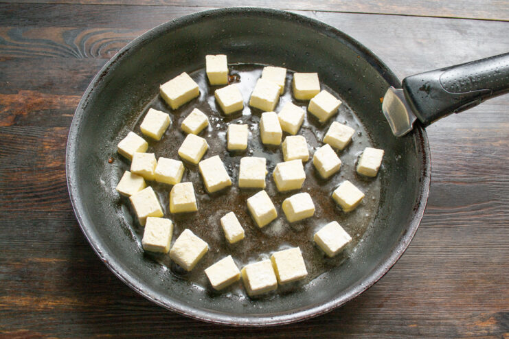 Frying Tofu Until Golden Brown Over High Heat Flour-coated tofu cubes frying in a hot pan to a golden brown color.