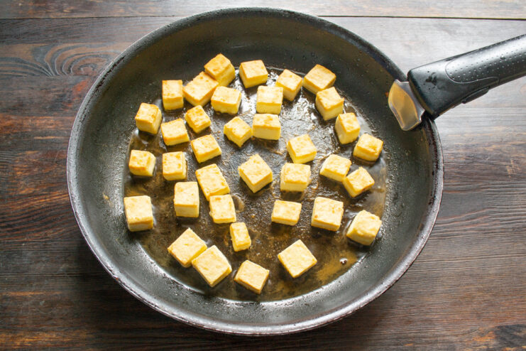 Flipping the Tofu to Fry the Other Side Golden-brown tofu cubes being flipped in a pan to cook evenly.