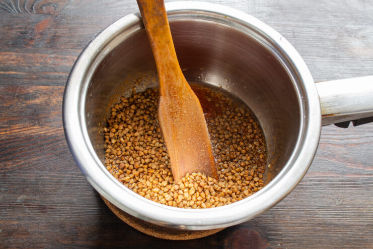 Adding Buckwheat Groats to the Pan Dry buckwheat groats being poured into the sauté pan with tomato sauce.