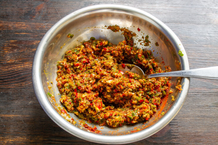 Mixing the Adjika Ingredients Thoroughly A spoon mixing the red adjika paste with spices in a white bowl.
