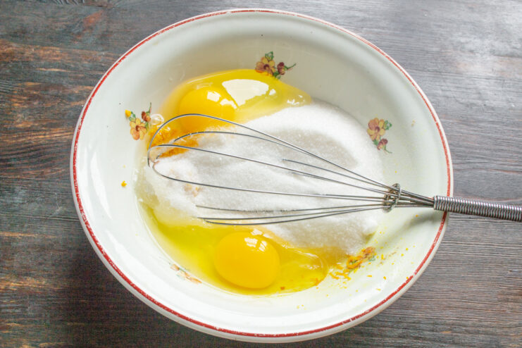 Starting the Cake Batter: Eggs and Sugar Cracking eggs into a glass bowl containing granulated sugar.