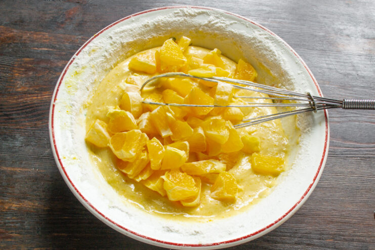 Adding Fresh Orange Pieces to the Batter Folding chopped orange pieces into the prepared cake batter in a bowl.
