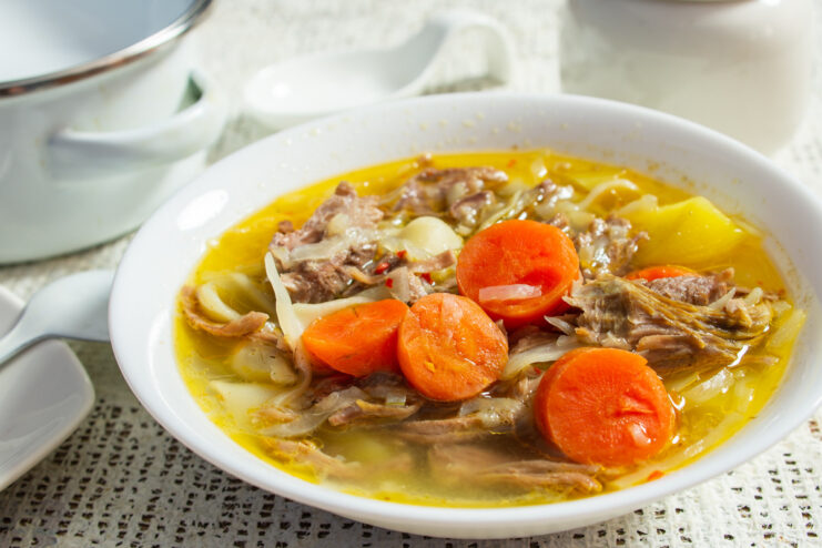 A bowl of Grandma's Soup with Meat and Pasta, garnished with fresh dill and a dollop of sour cream.