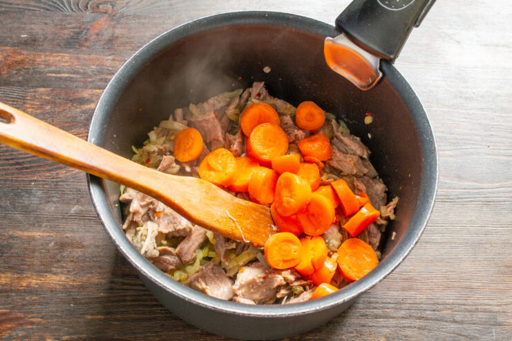Adding thick carrot slices to the soup pot. Thickly sliced carrots being added to the pot with meat and onions.