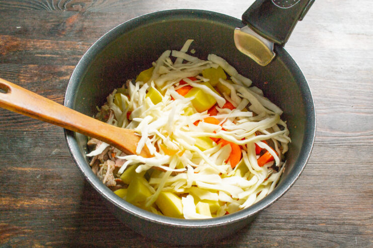 Adding shredded cabbage to the meat and vegetable soup. Thinly shredded cabbage being added to the pot for the soup.