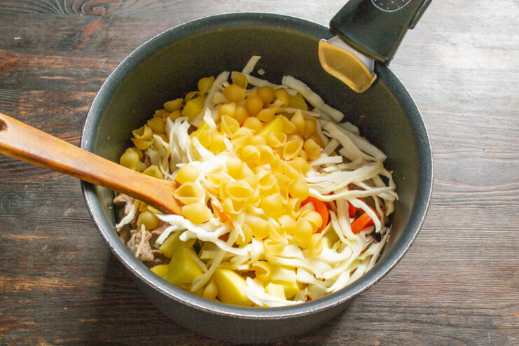 Adding small pasta to the soup. A hand pouring small pasta into the soup pot.