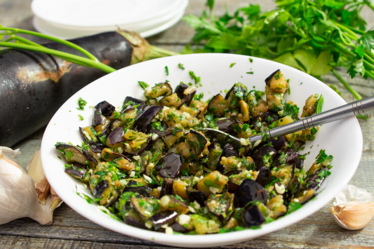 A white bowl filled with fried eggplant cubes mixed with garlic and fresh parsley.
