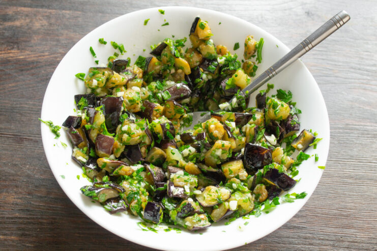Finishing the Dish with a Splash of Vinegar Mixing fried eggplant, garlic, and parsley in a bowl after adding vinegar.
