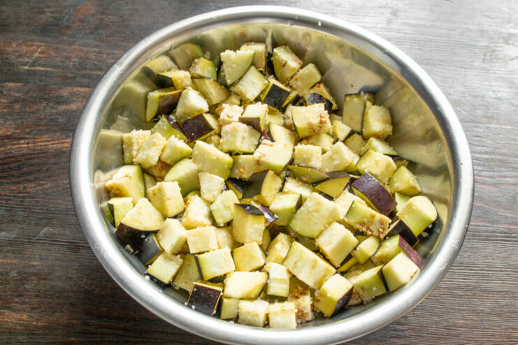 Tossing the Eggplant Cubes with Salt A close-up of diced eggplant being mixed with salt in a clear bowl.