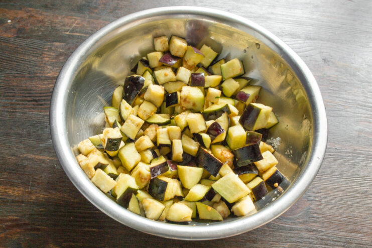 Pressing the Eggplant to Release Excess Water A bowl of salted eggplant is pressed down with a plate and a jar of water on top.