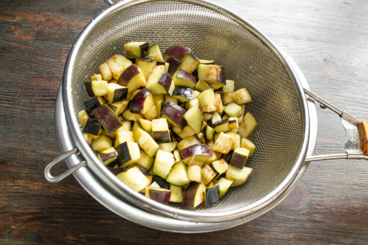 Rinsing the Salted Eggplant Before Frying Rinsing diced eggplant in a metal sieve under running water from a tap.