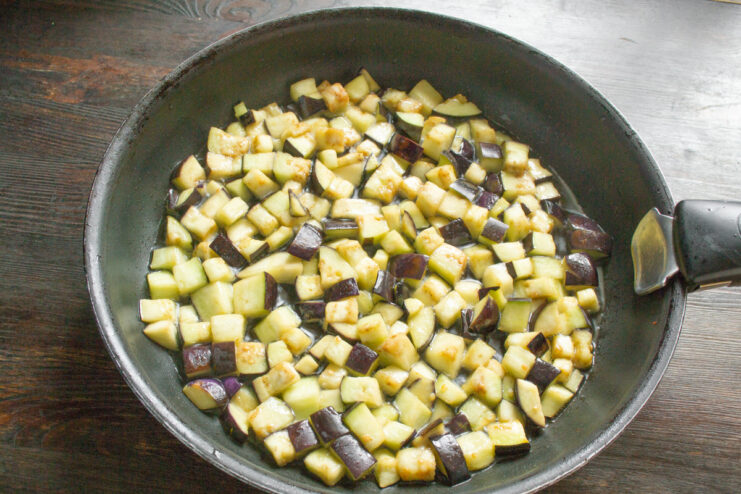 Adding Dried Eggplant Cubes to a Hot Skillet Dried eggplant cubes being added from a bowl into a hot skillet with oil.
