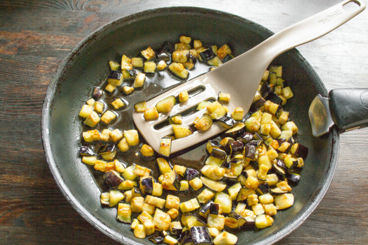 Frying the Eggplant Until Perfectly Golden Brown Eggplant cubes being fried to a golden-brown color in a black skillet.