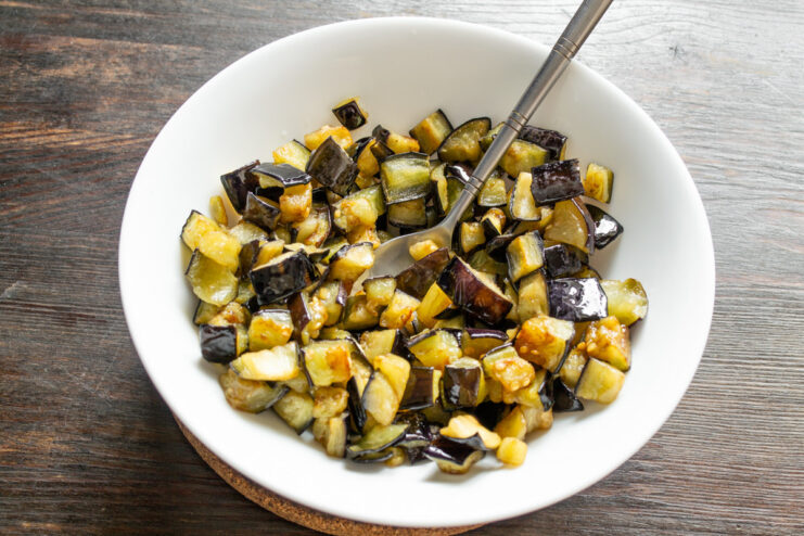 Removing Fried Eggplant with a Slotted Spoon to Drain Oil A slotted spoon lifting golden-fried eggplant cubes out of a skillet.