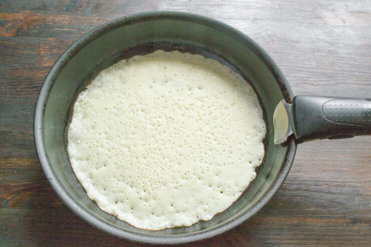 Cooking the Thin Blinchiki Crepes Pouring thin batter from a ladle into a hot skillet to cook a blinchik.