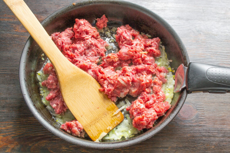 Adding Ground Beef to the Sautéed Onions Adding a block of raw ground beef to the skillet with sautéed onions.